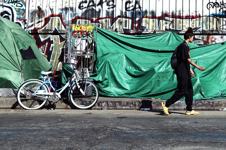 A person walks past an encampment of unhoused people in the Skid Row community on in Los Angeles.